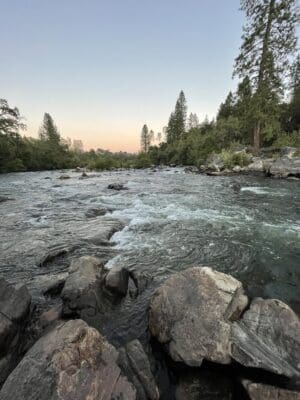 Scenic view of the South Fork river at dusk, showcasing gentle rapids over rocks and surrounding greenery, symbolizing ongoing river conservation efforts and the natural beauty being protected.