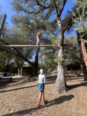 Young participants engaged in an outdoor ropes course activity at Mother Lode River Center, showcasing teamwork and adventure under a clear blue sky.